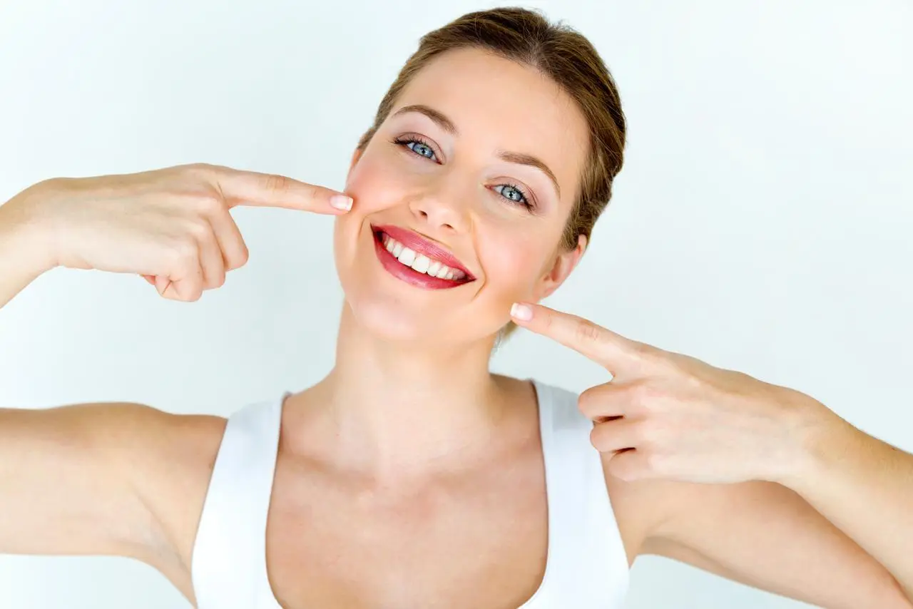 A smiling patient pointing at her straightened teeth
