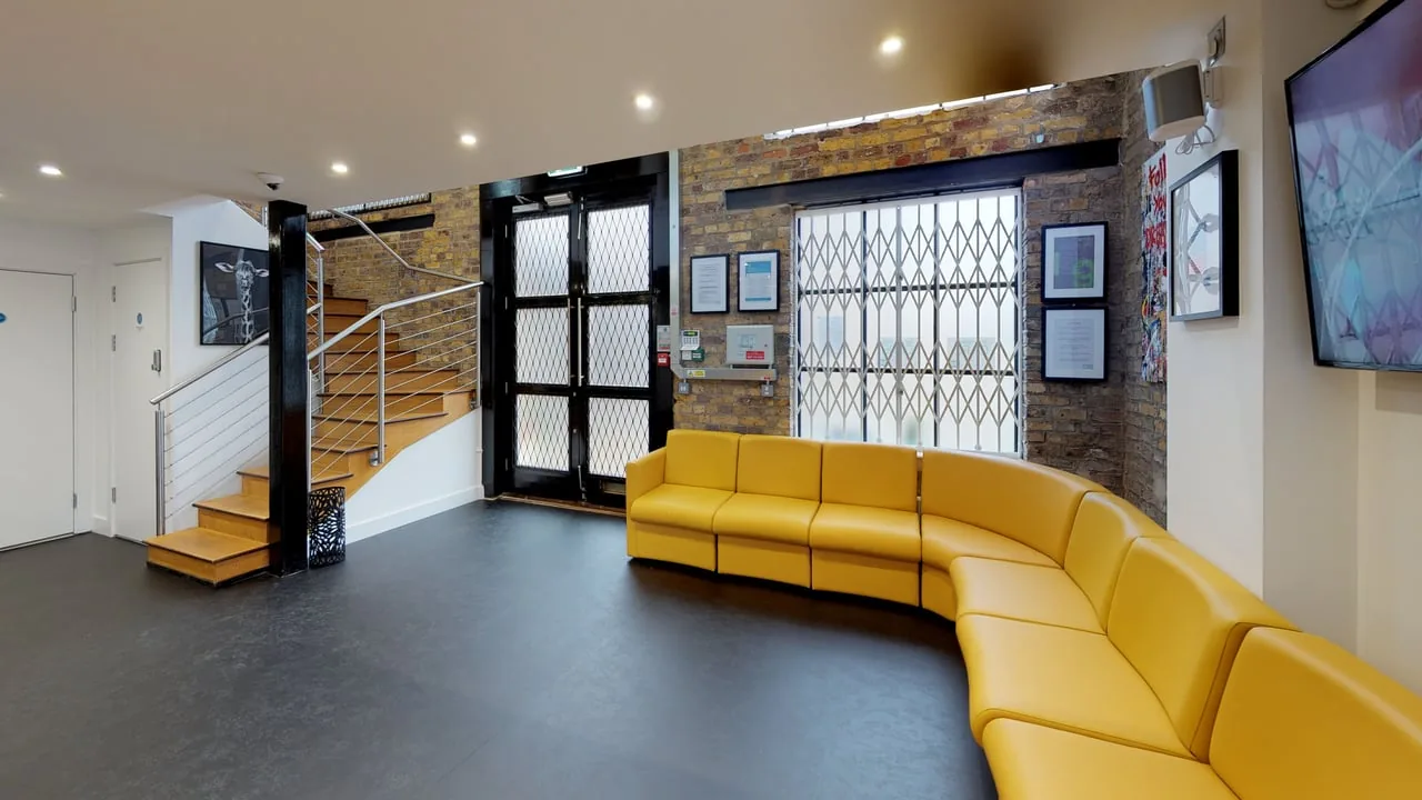 Reception at our Brentford practice —
            exposed brick, a curved yellow sofa and a timber staircase